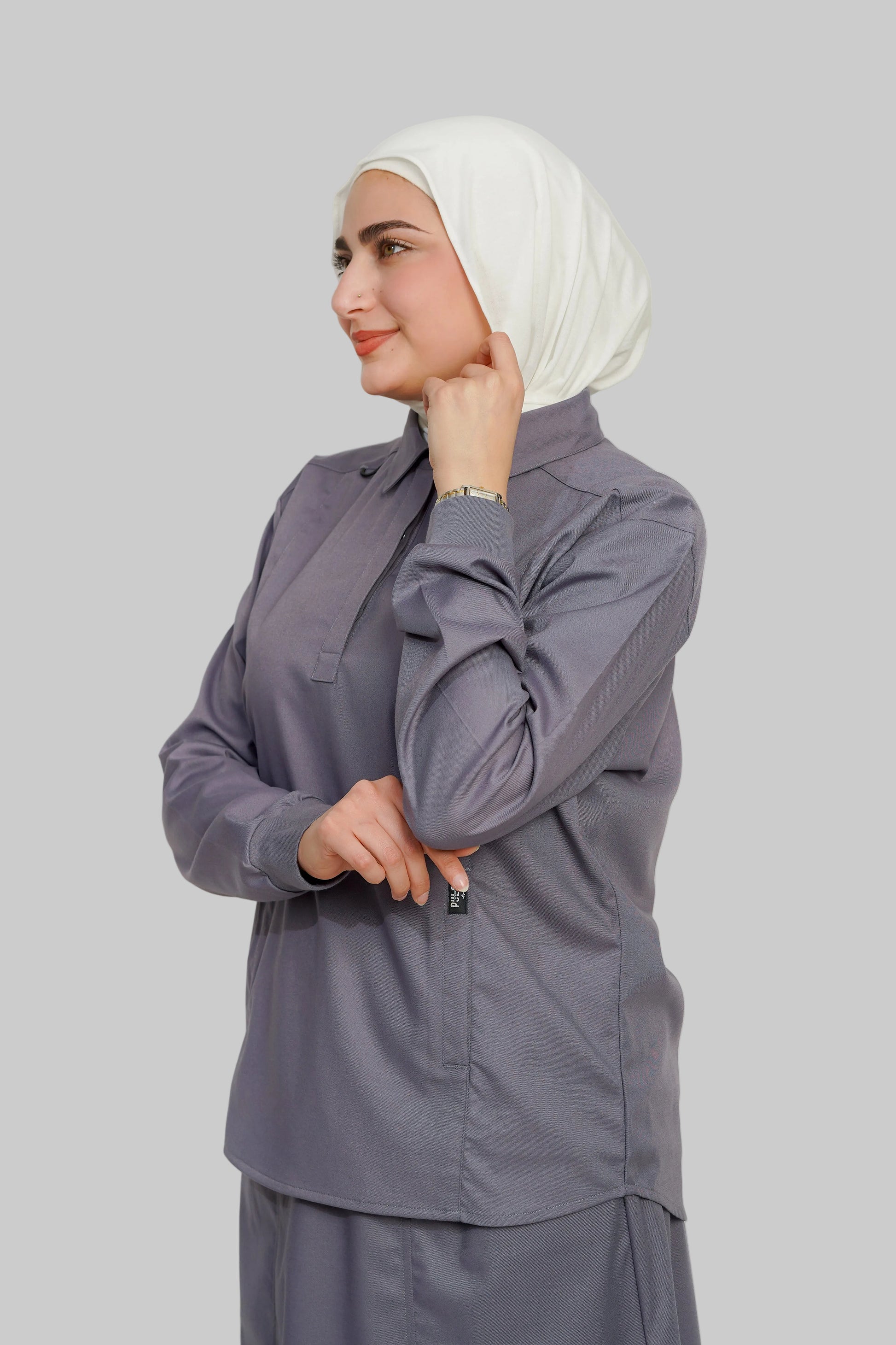 Woman wearing a gray outfit with a white hijab against a plain background