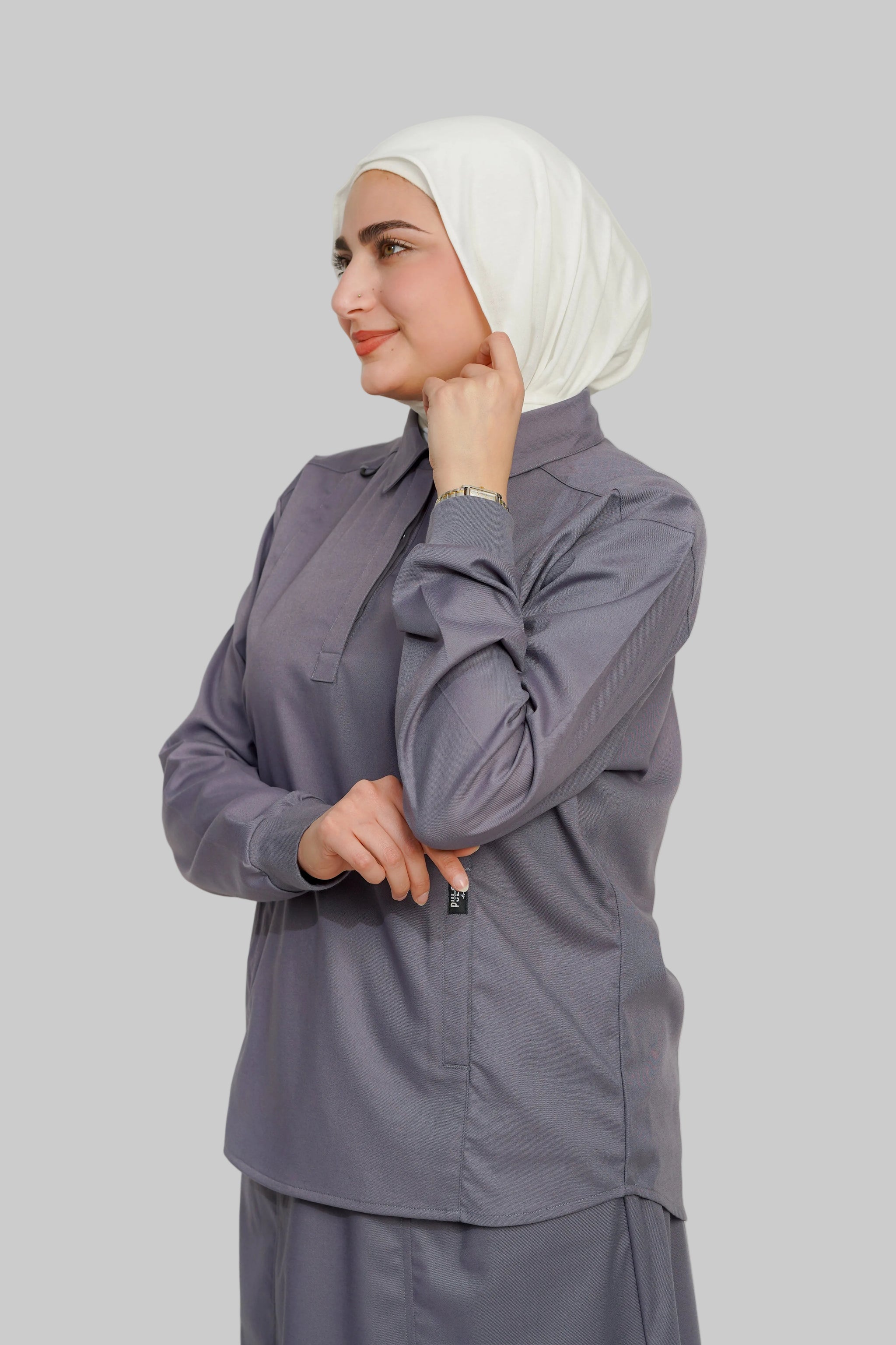 Woman wearing a gray outfit with a white hijab against a plain background