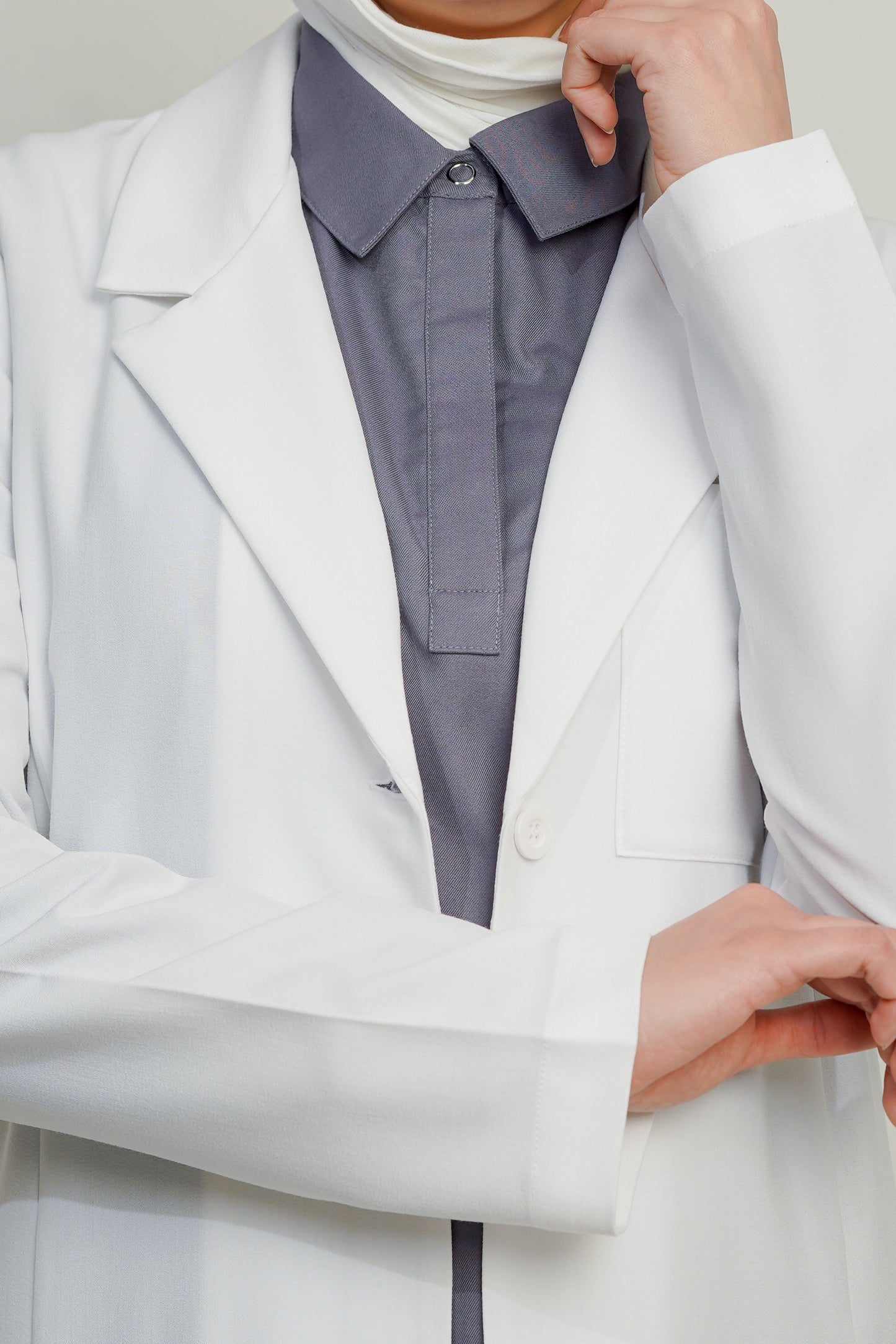 Close-up of a person wearing a light gray blazer over a white turtleneck.