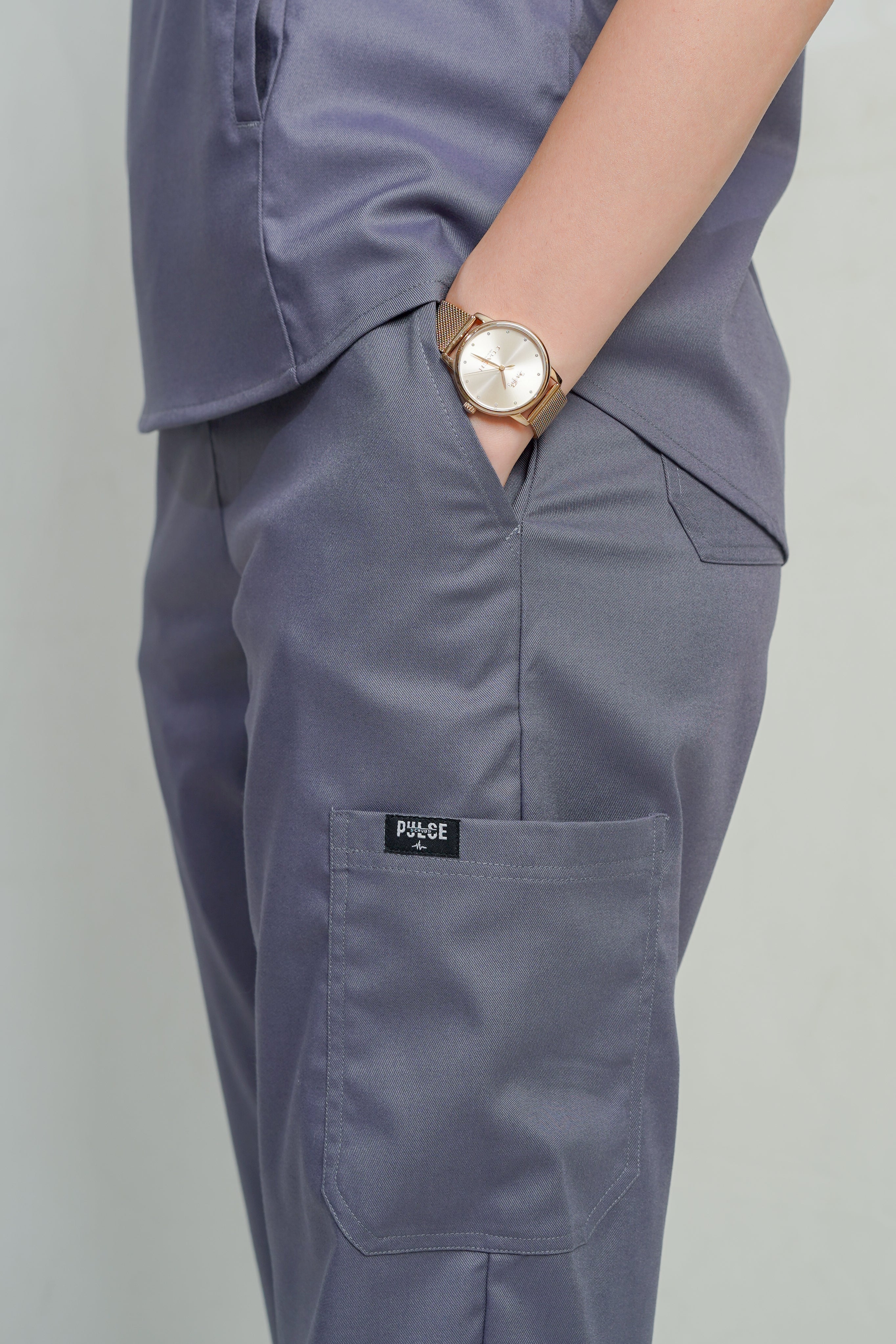 Person wearing gray pants with a visible brand logo on a plain background