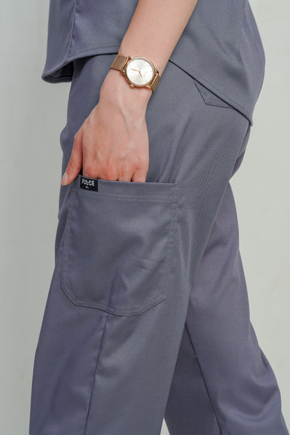 Person wearing a gray scrub set with a gold watch on a plain background