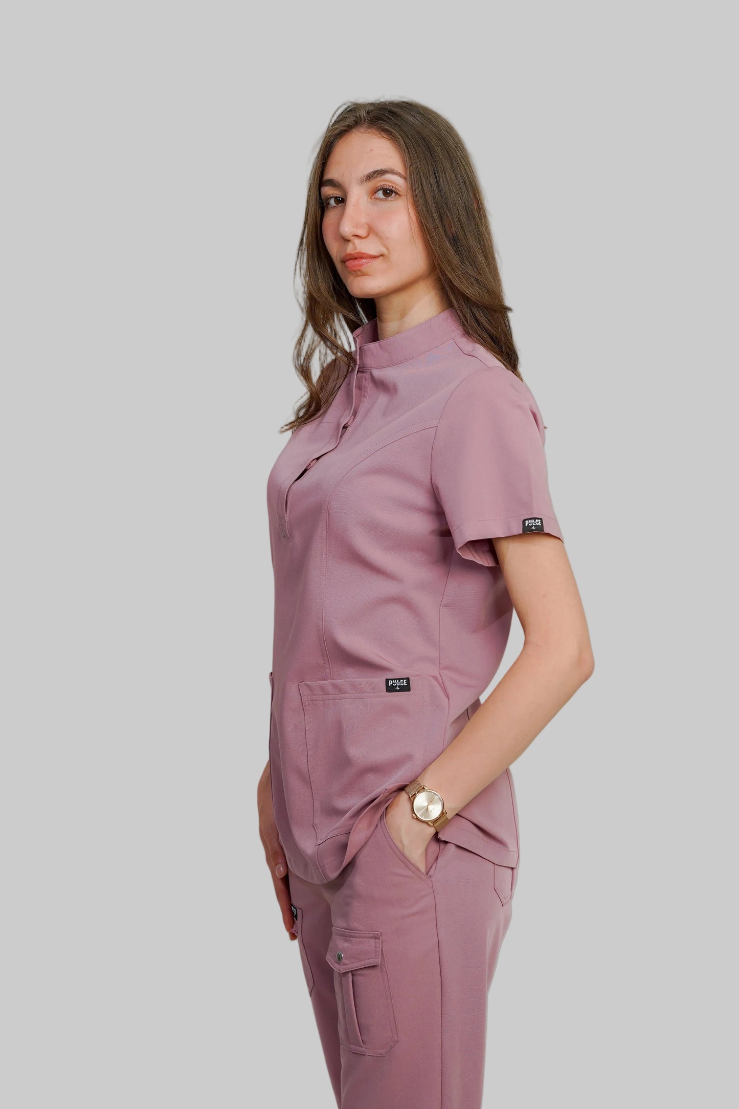 Woman wearing a matching pink scrub set against a plain background