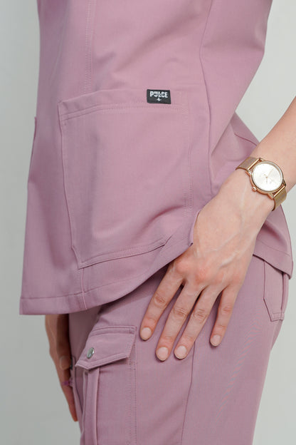 Person wearing a light purple scrub set with a visible brand logo, holding a wristwatch.