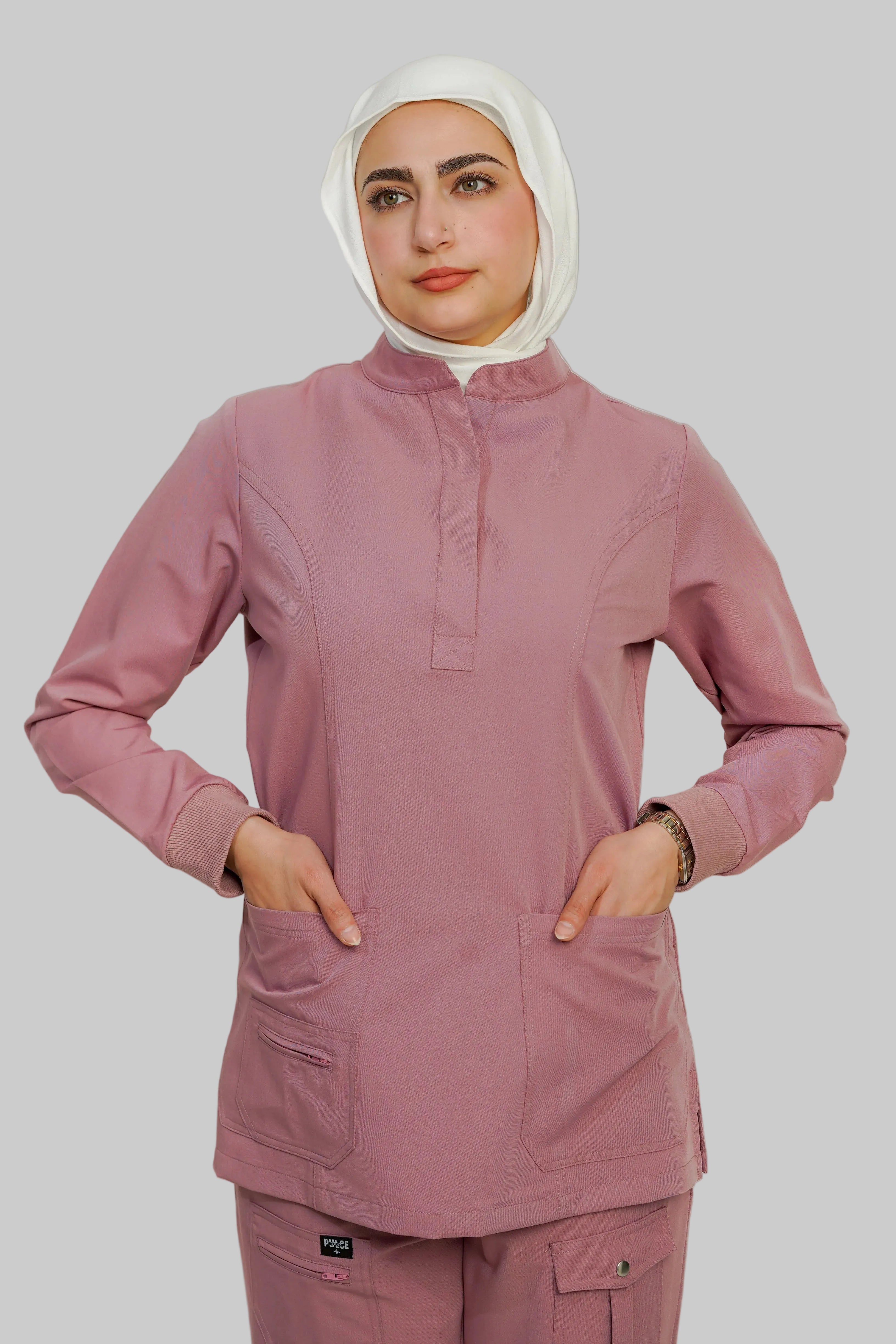Person wearing a pink scrub set with a hijab on a plain background