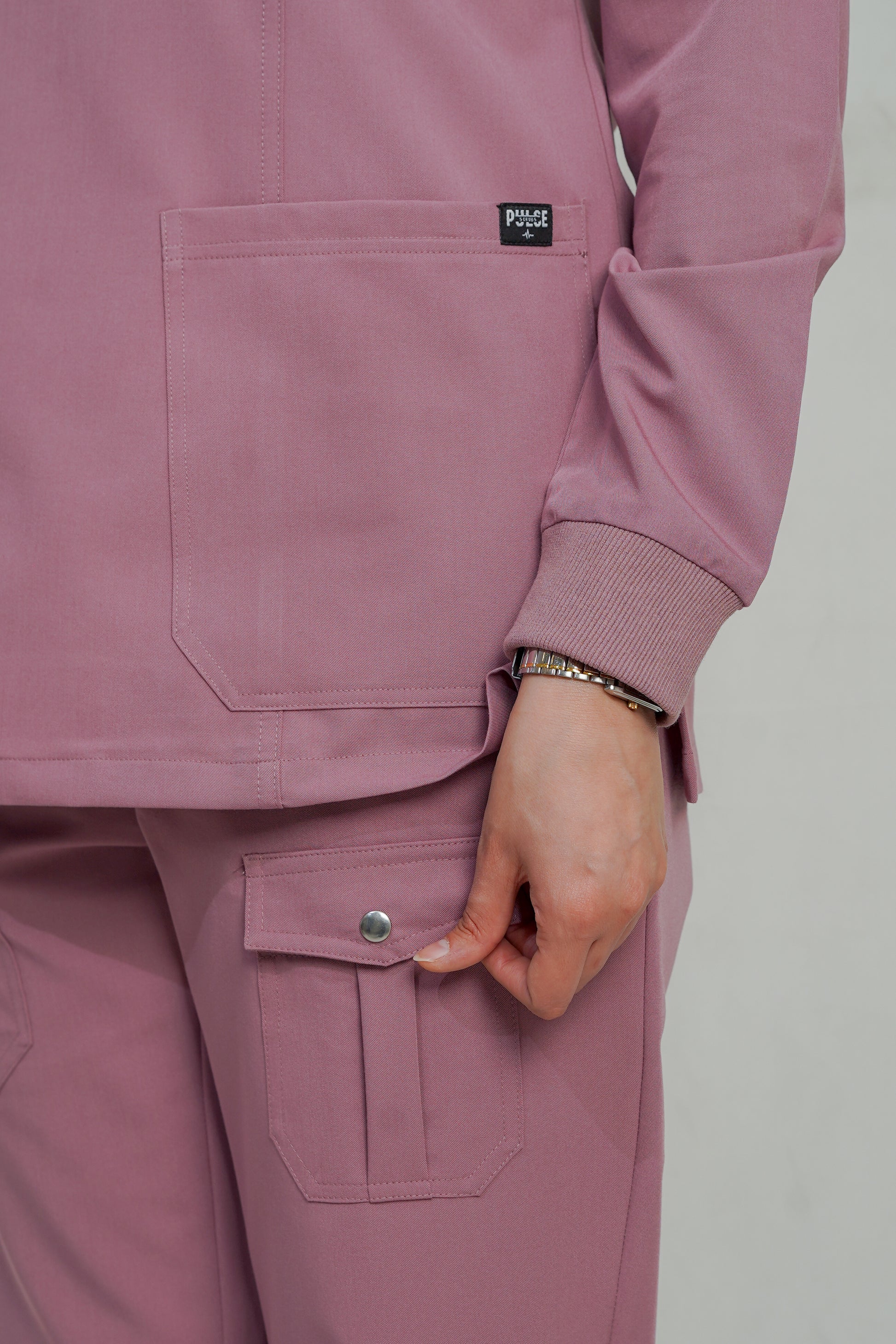 Close-up of a person wearing a pink scrub set with a visible brand logo on a plain background