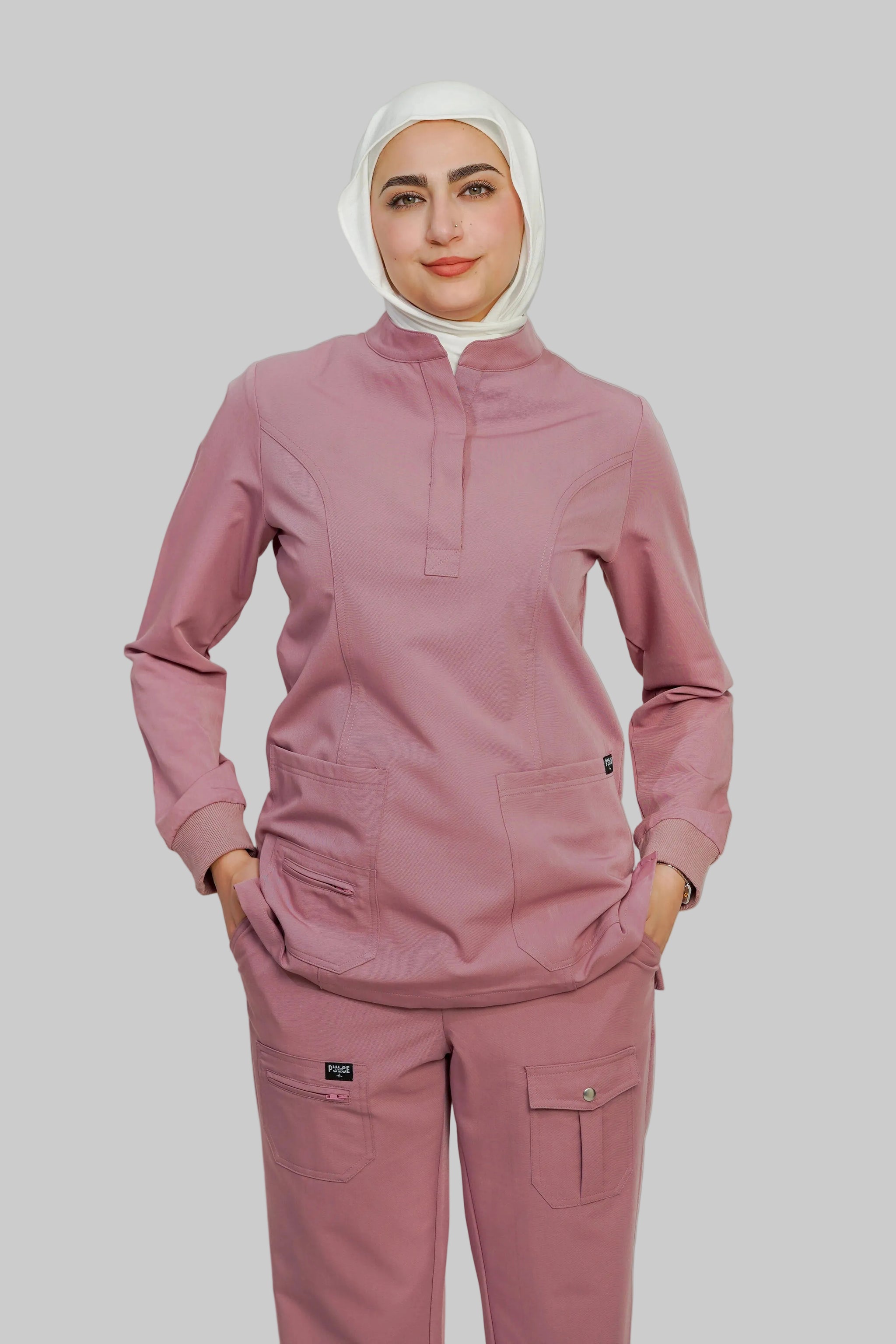 Person wearing a pink scrub set with a white hijab on a plain background