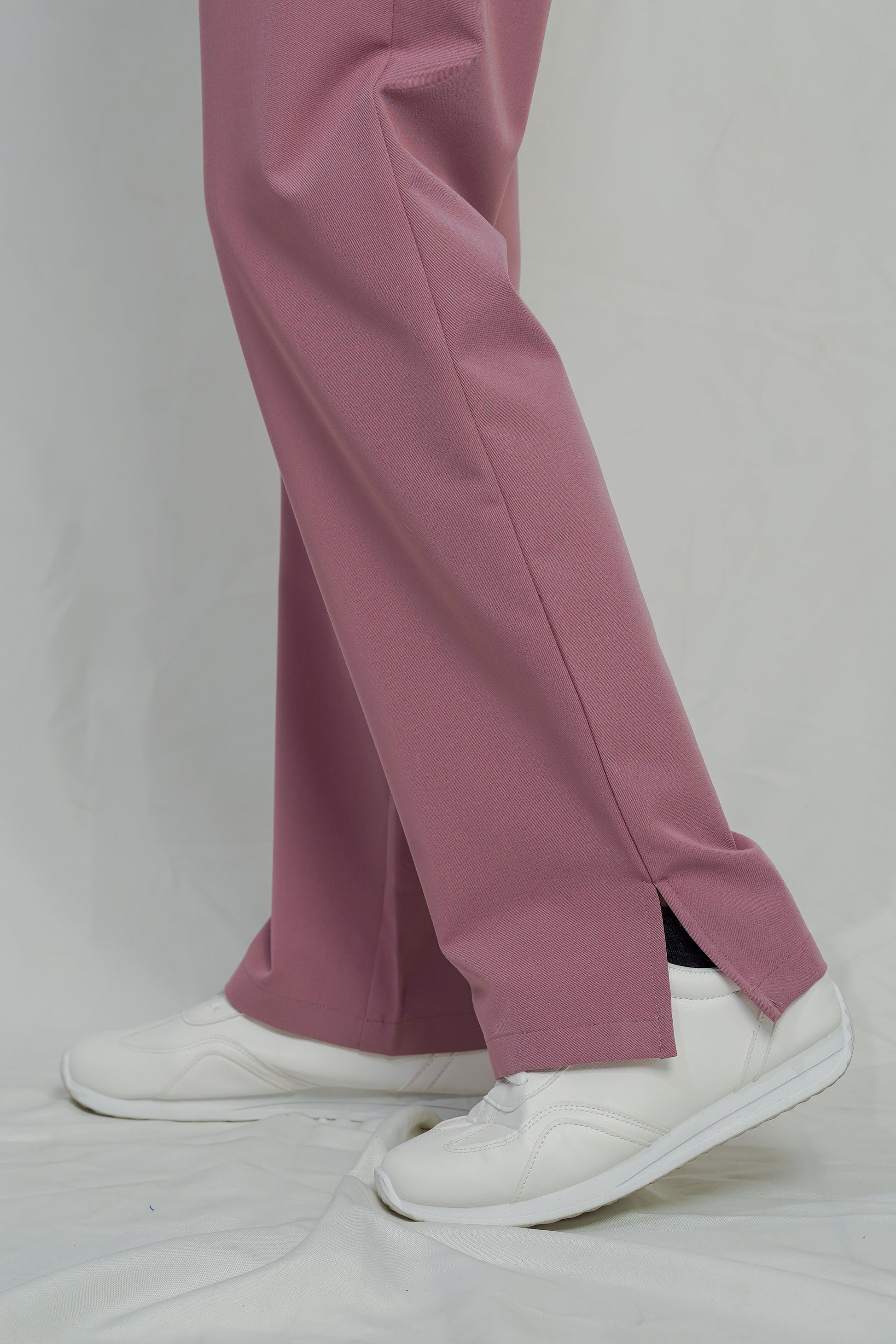 Pink pants worn with white sneakers on a plain background