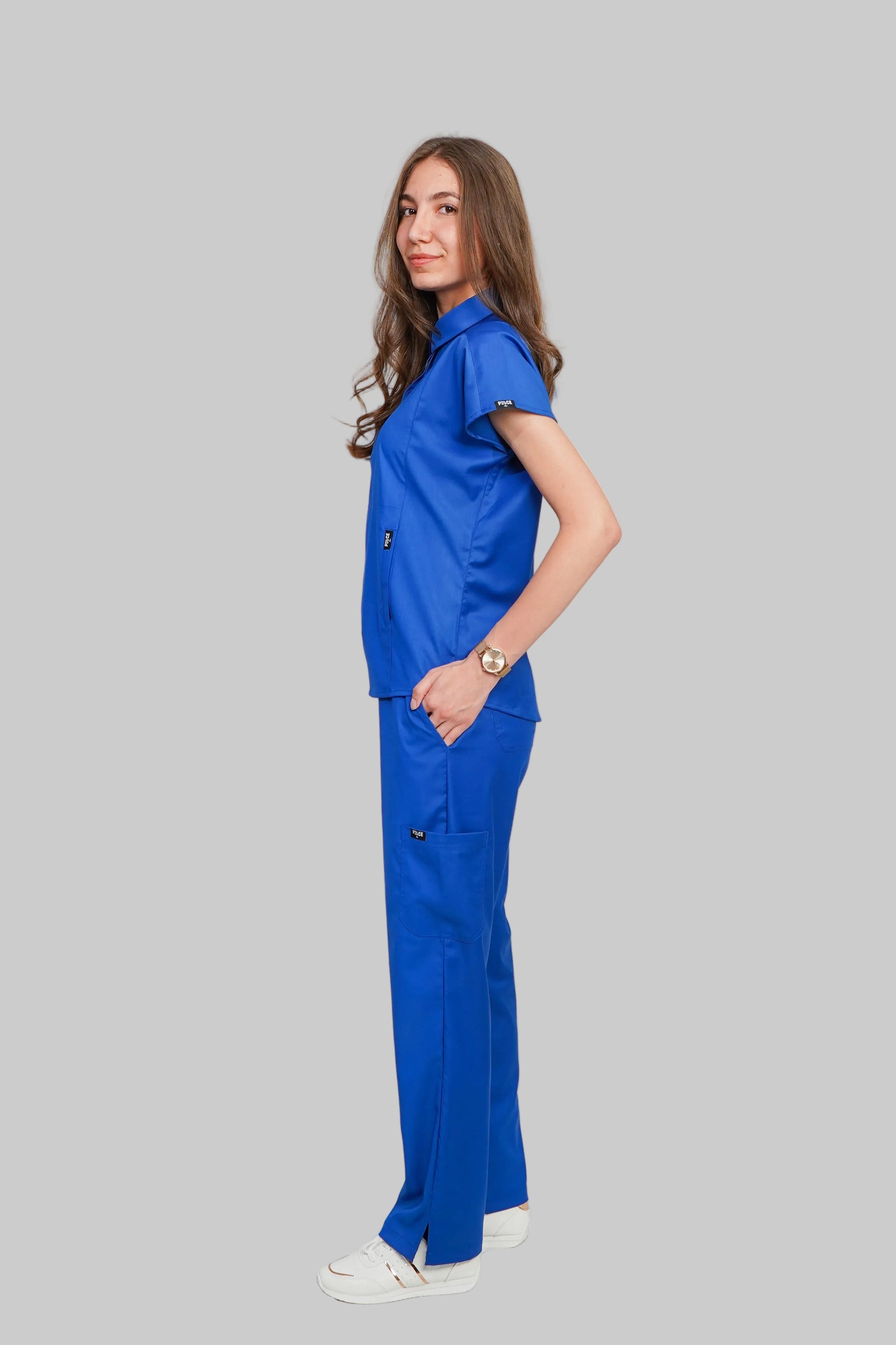 Woman wearing a blue medical scrub set against a white background