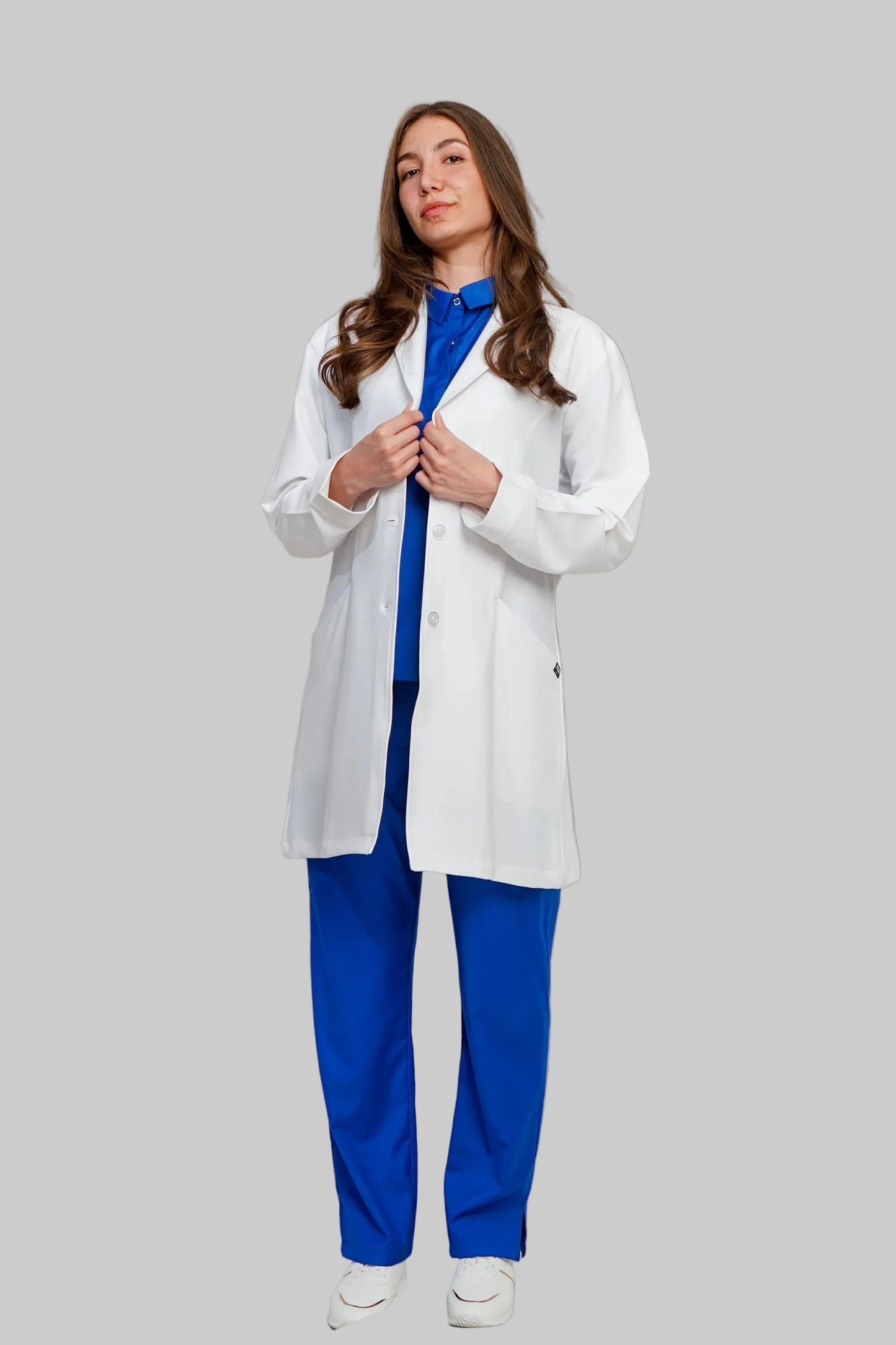 Person wearing a white coat over blue scrubs on a plain background