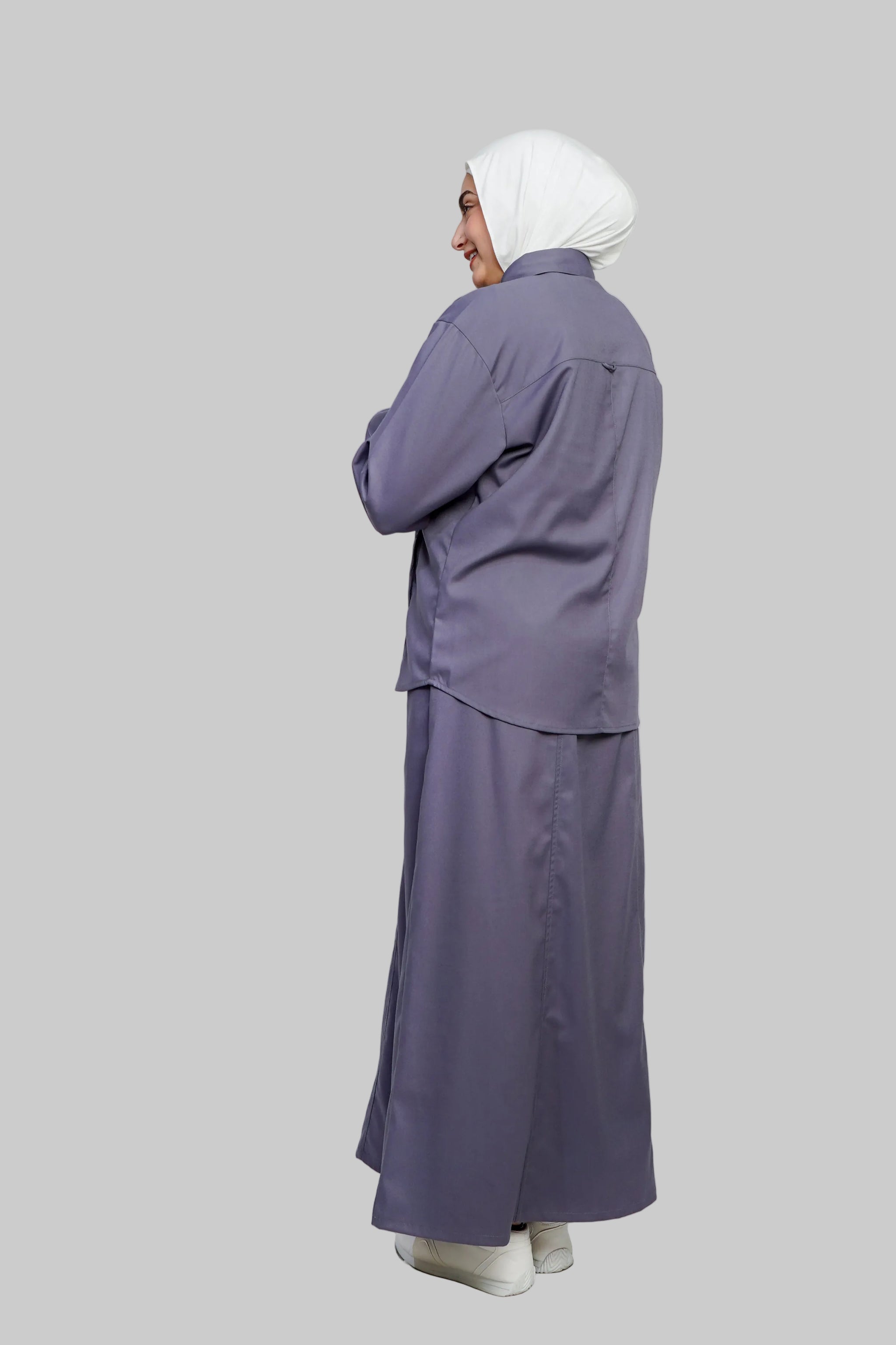 Person wearing a long purple outfit with a white headscarf on a light gray background