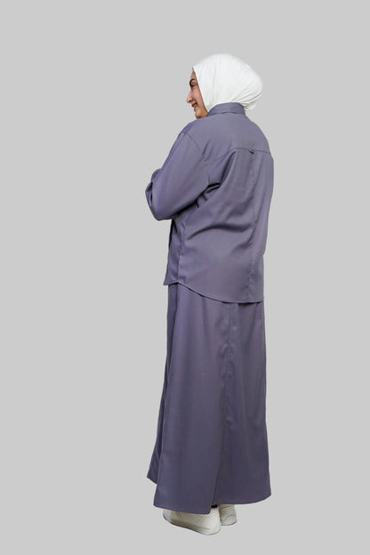 Person wearing a long purple outfit with a white headscarf on a light gray background