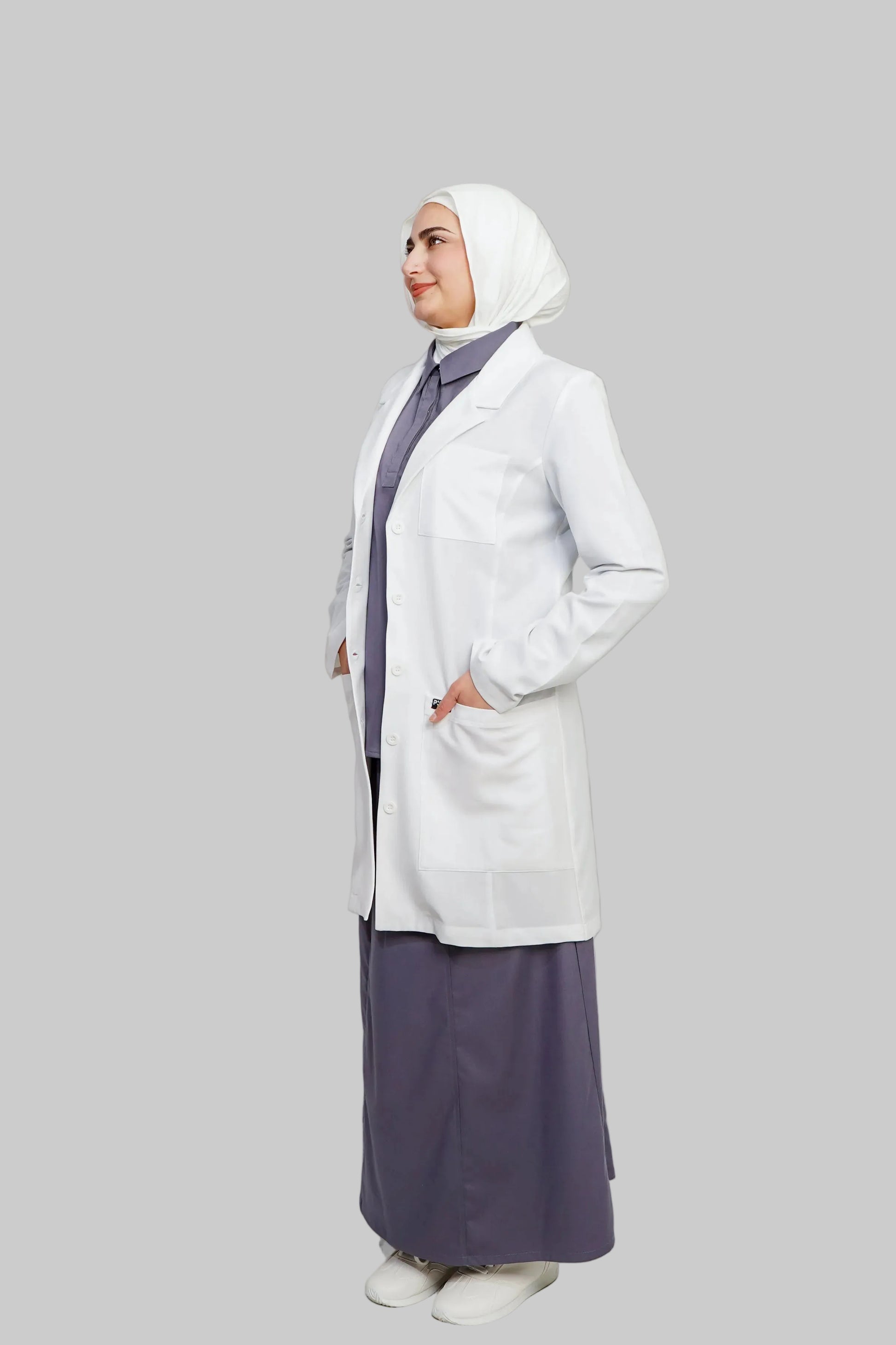 Woman wearing a white lab coat over a purple outfit on a plain background
