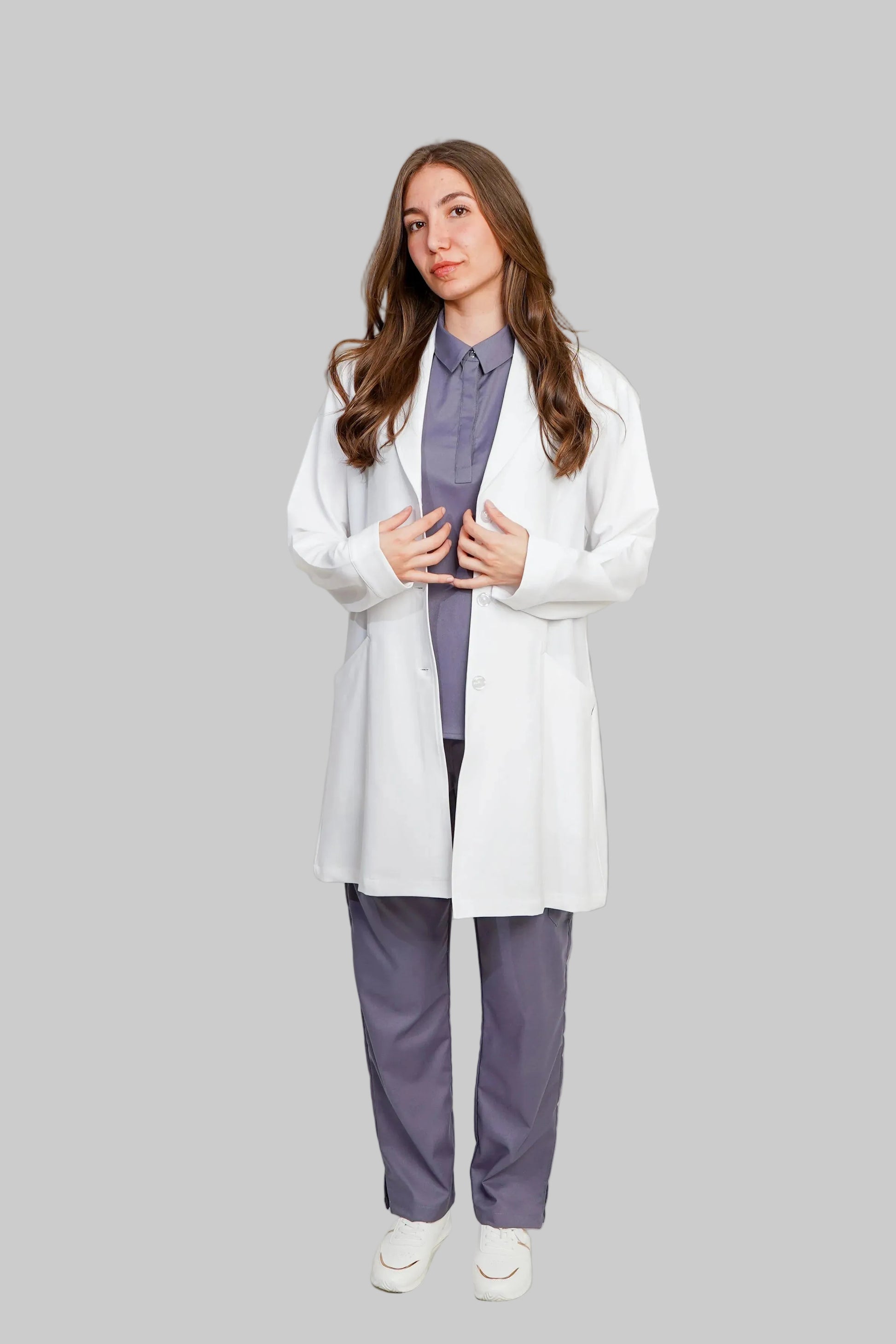 Person wearing a white lab coat over a purple shirt and pants on a light gray background