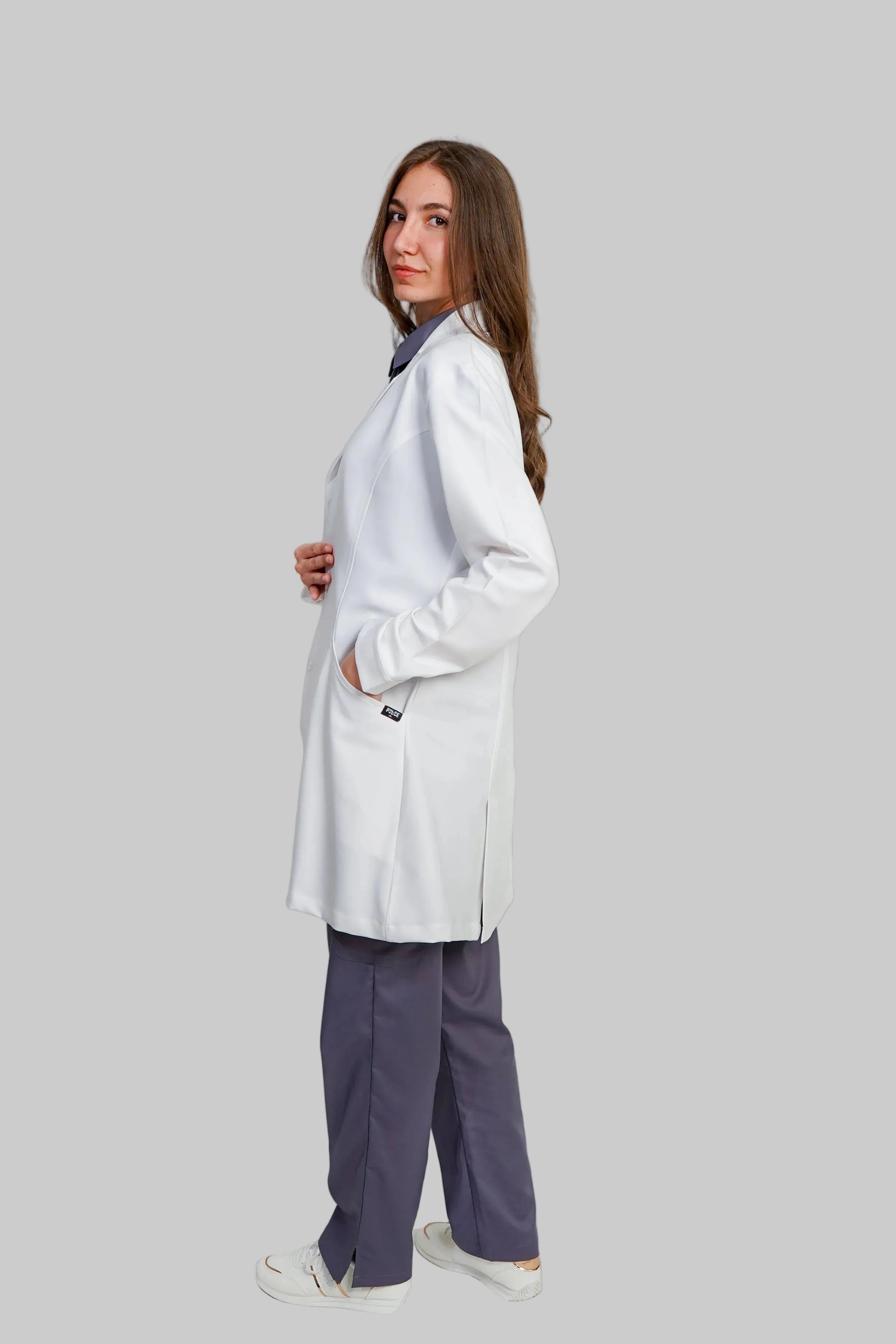 Person wearing a white lab coat and purple pants on a plain background
