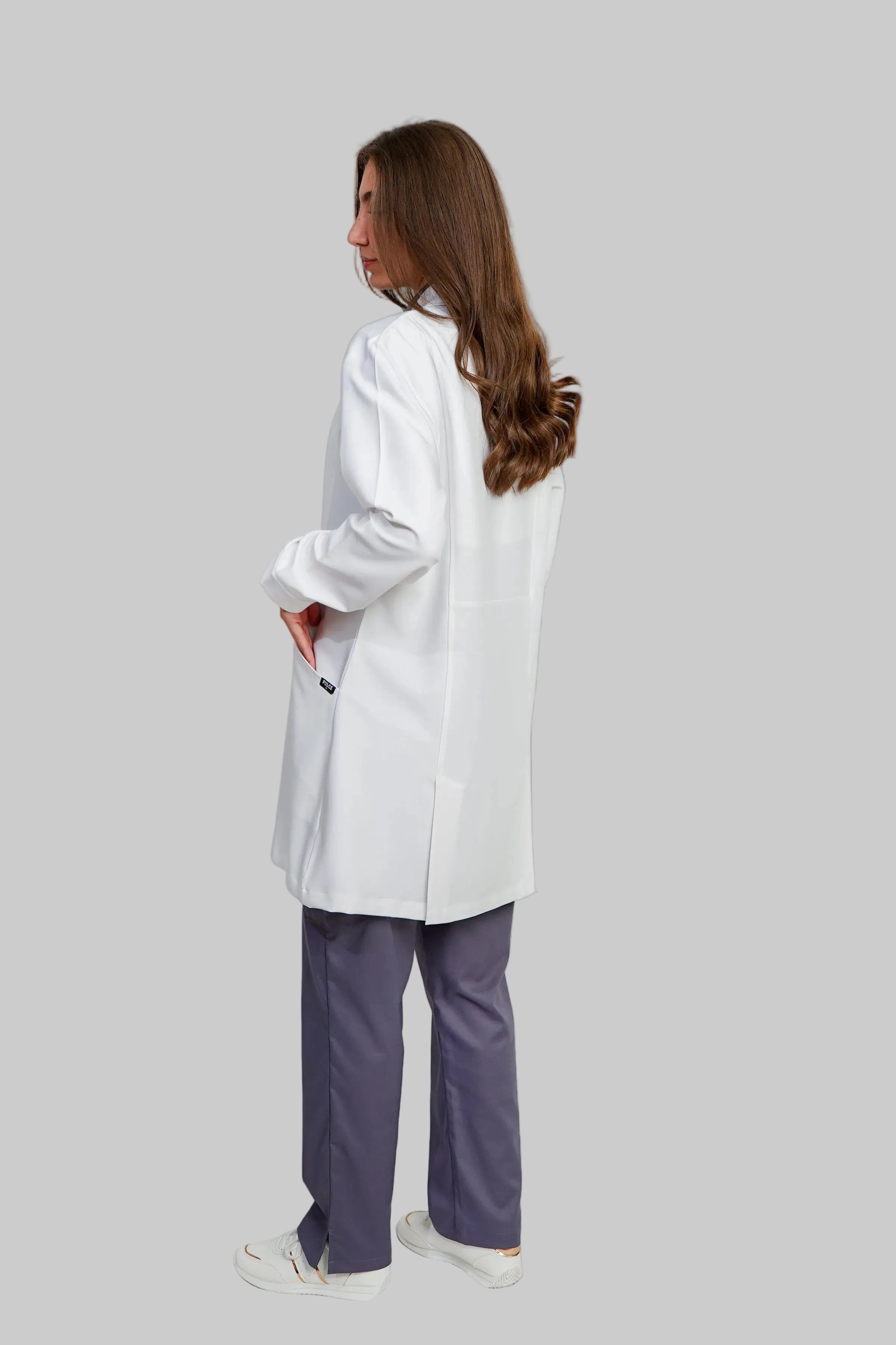 Person wearing a white lab coat and purple pants on a plain background