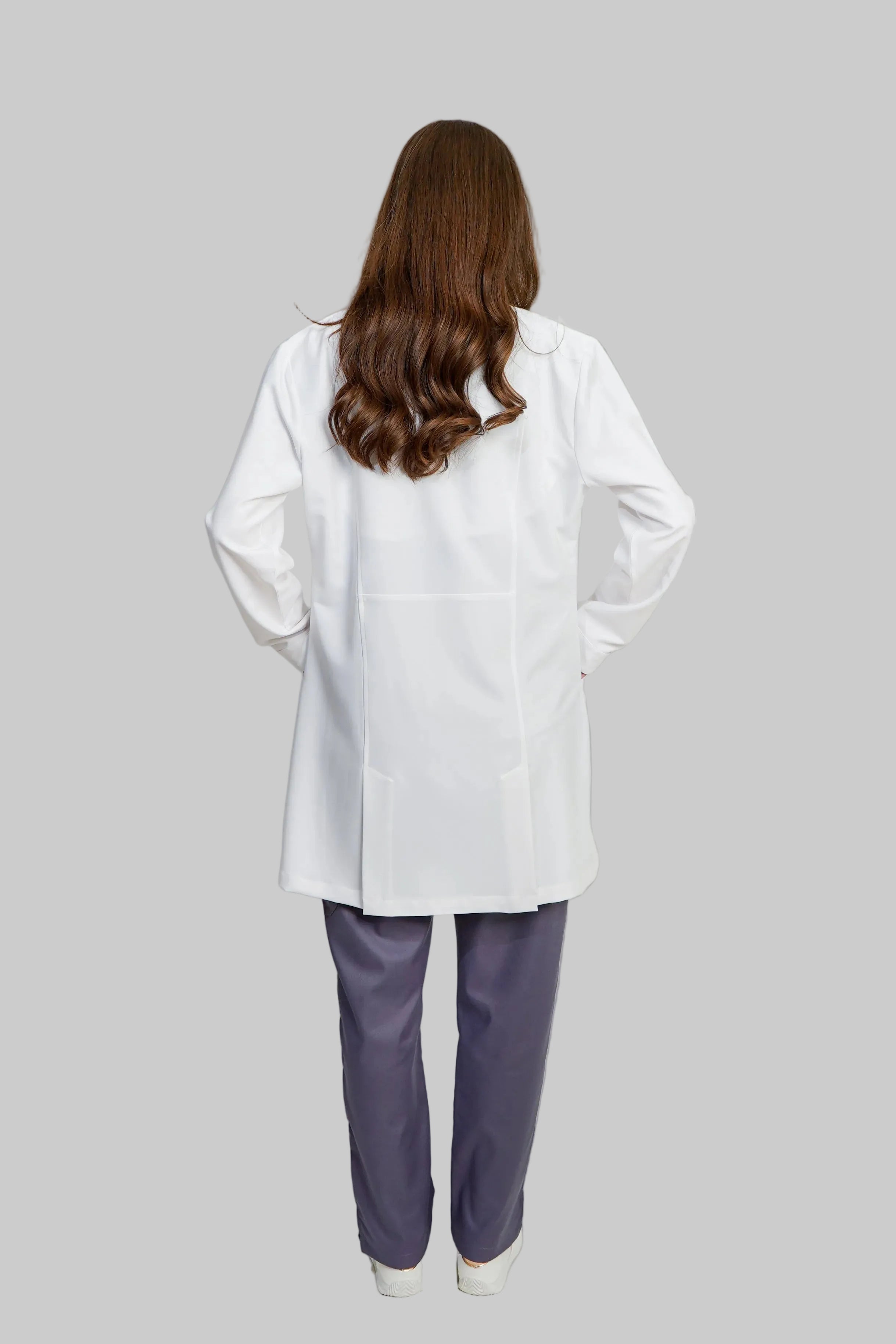 Person wearing a white lab coat and purple pants on a plain background