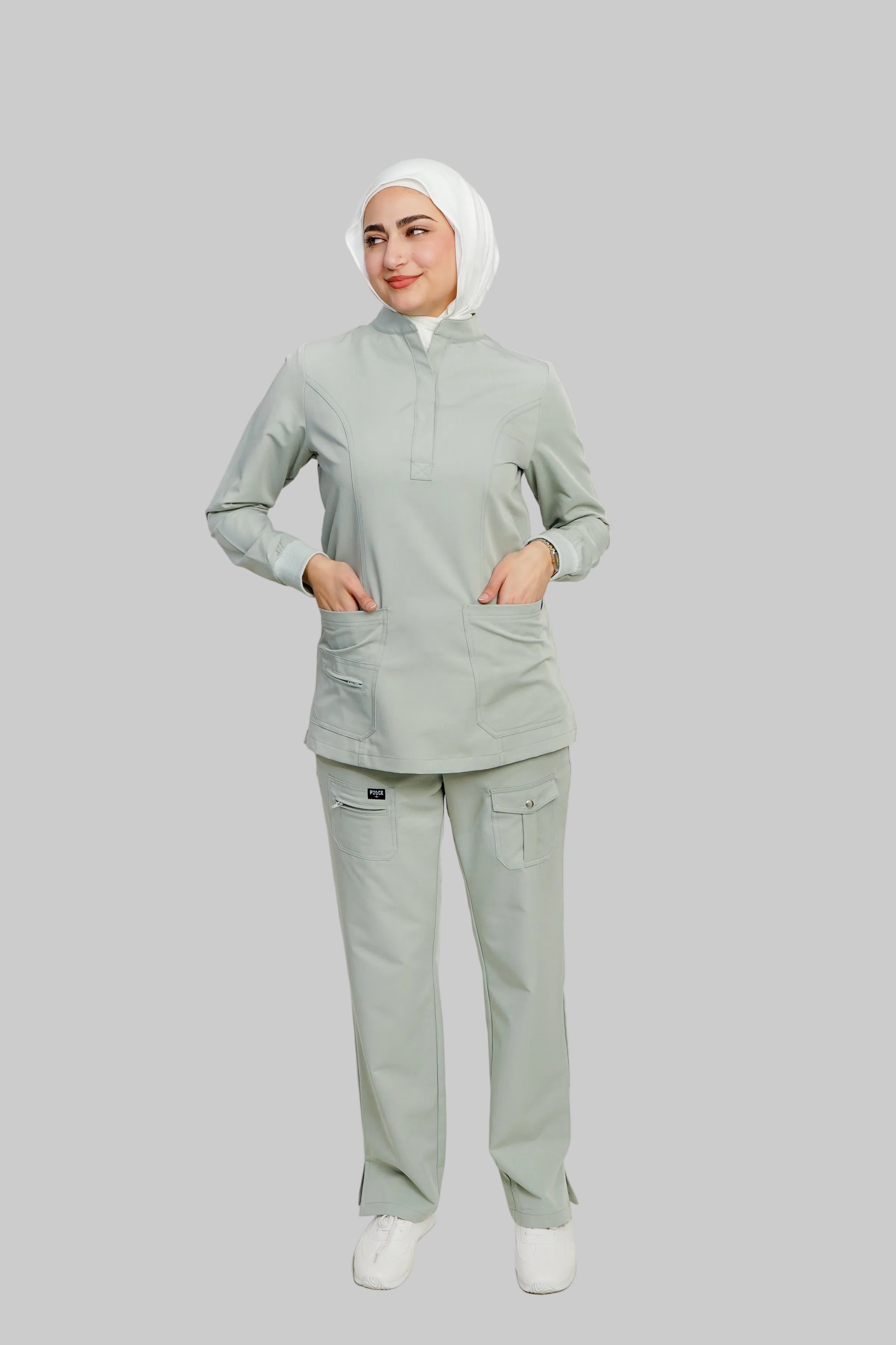 Person wearing a light gray scrub set with a white hijab on a plain background