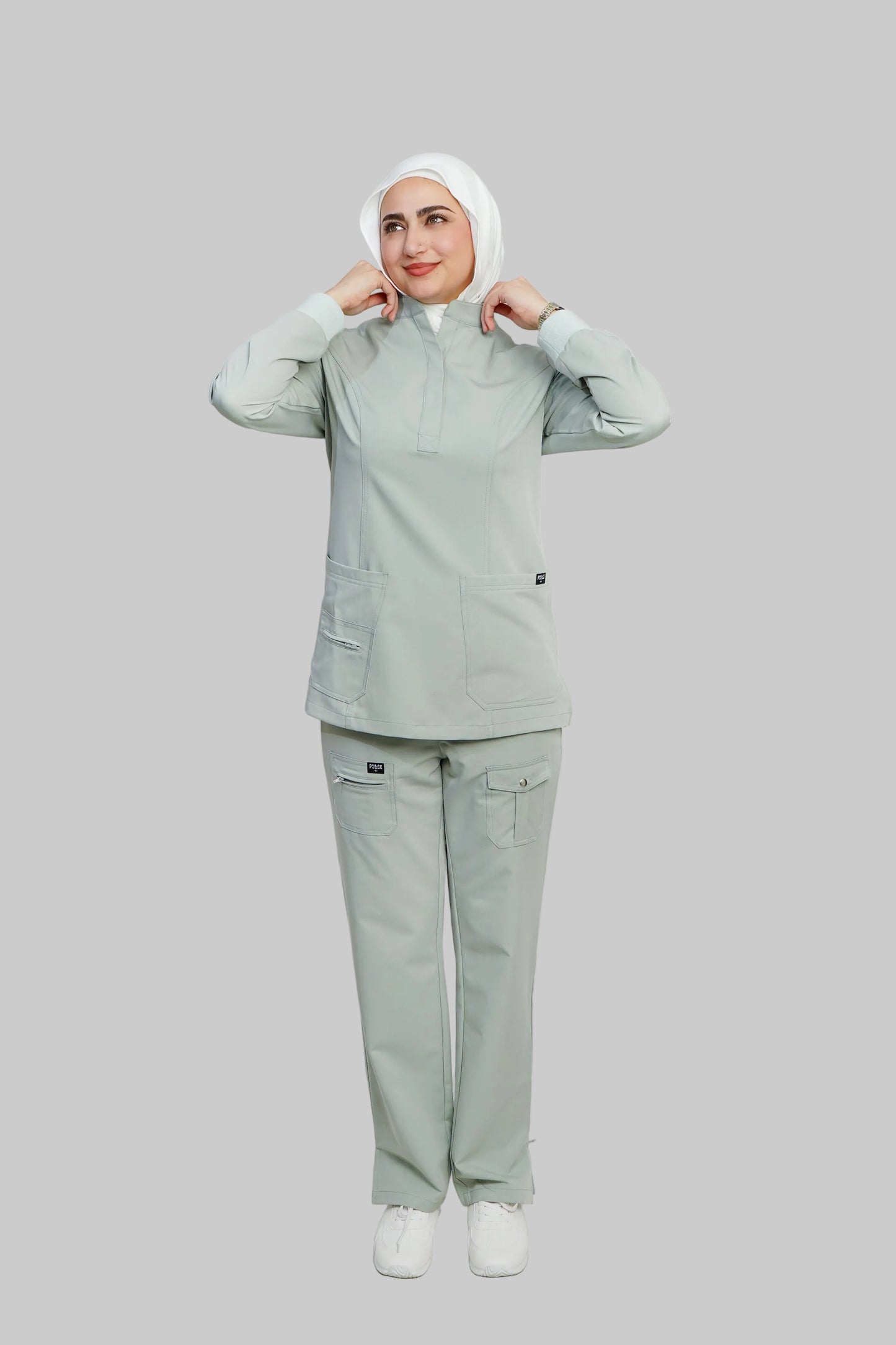 Person wearing a light gray medical uniform with a headscarf on a white background