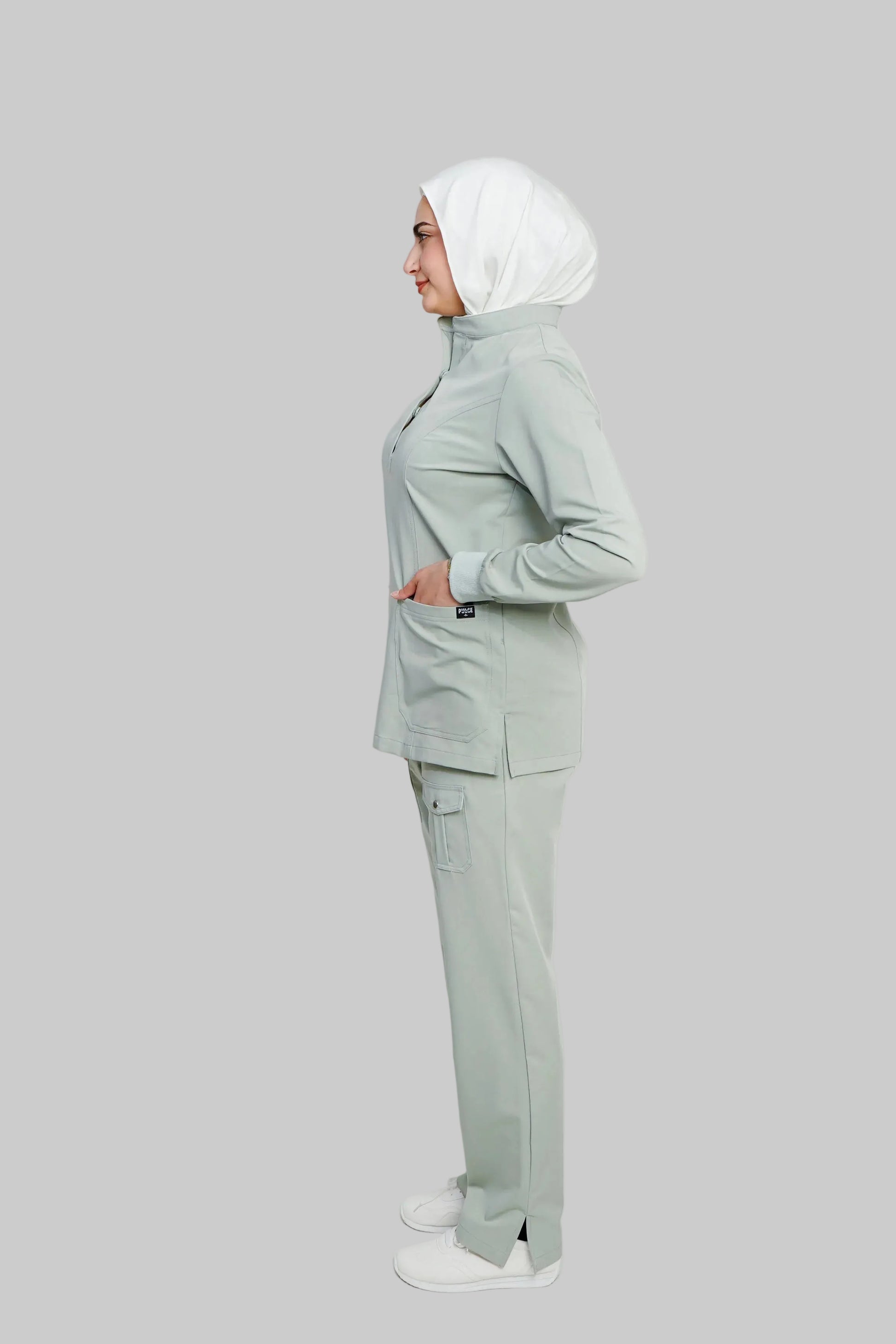 Woman wearing a light gray outfit with a hijab on a white background