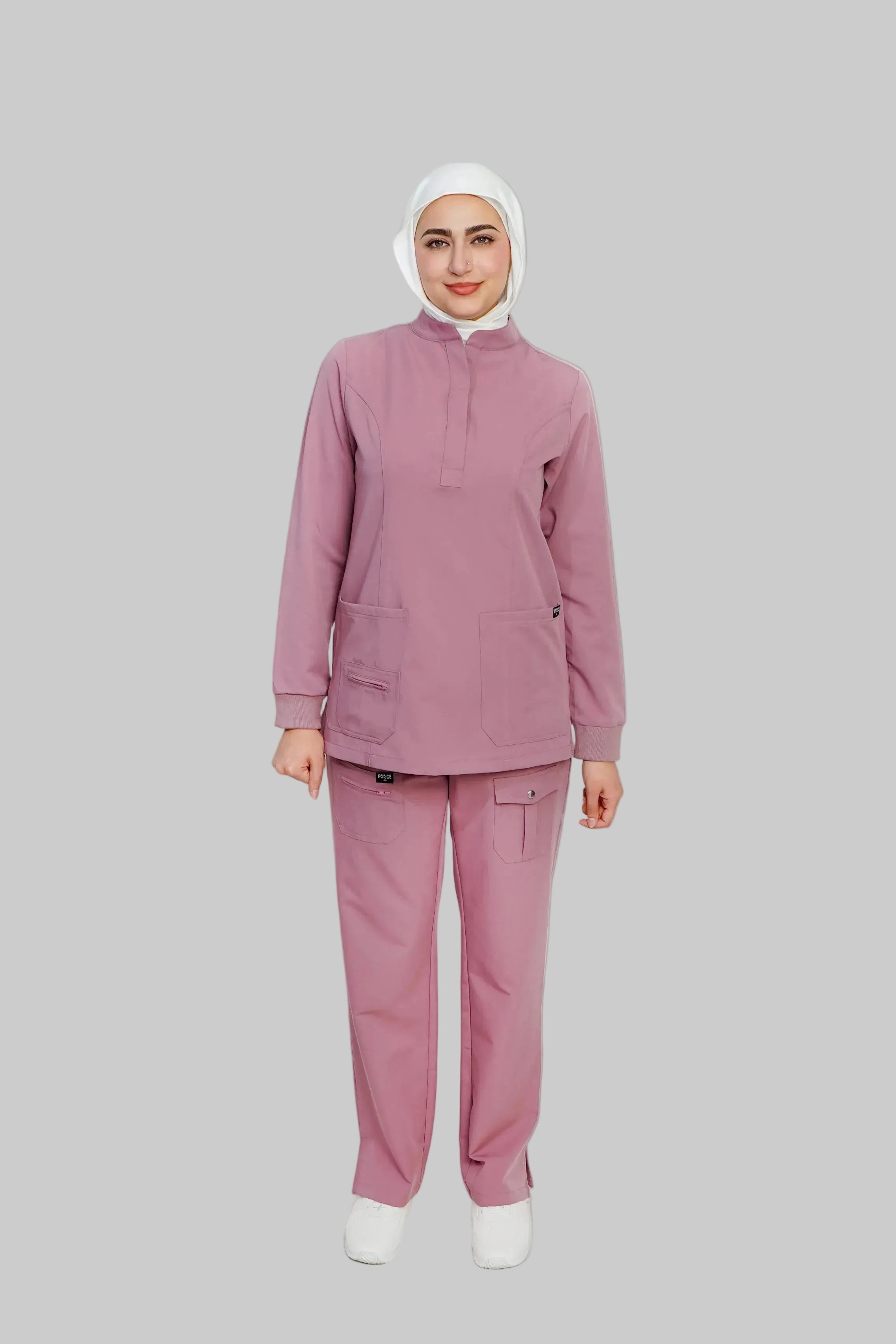 Person wearing a pink medical uniform with a white hijab on a light gray background