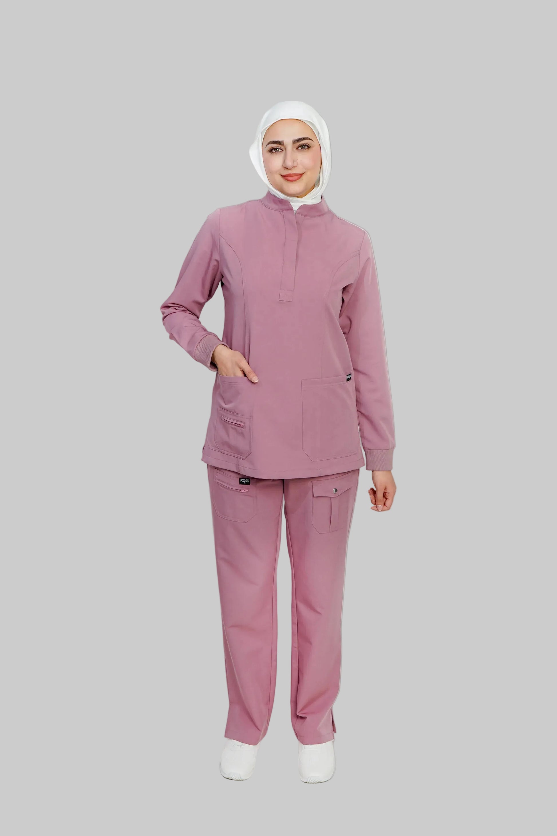 Person wearing a pink medical scrub set with a white hijab on a light gray background