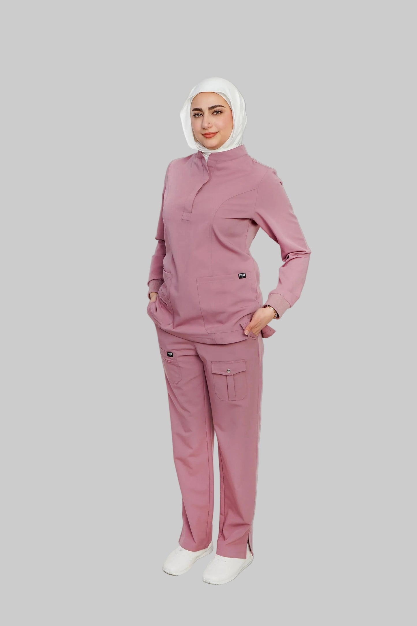 Person wearing a pink tracksuit with a white hijab on a light gray background