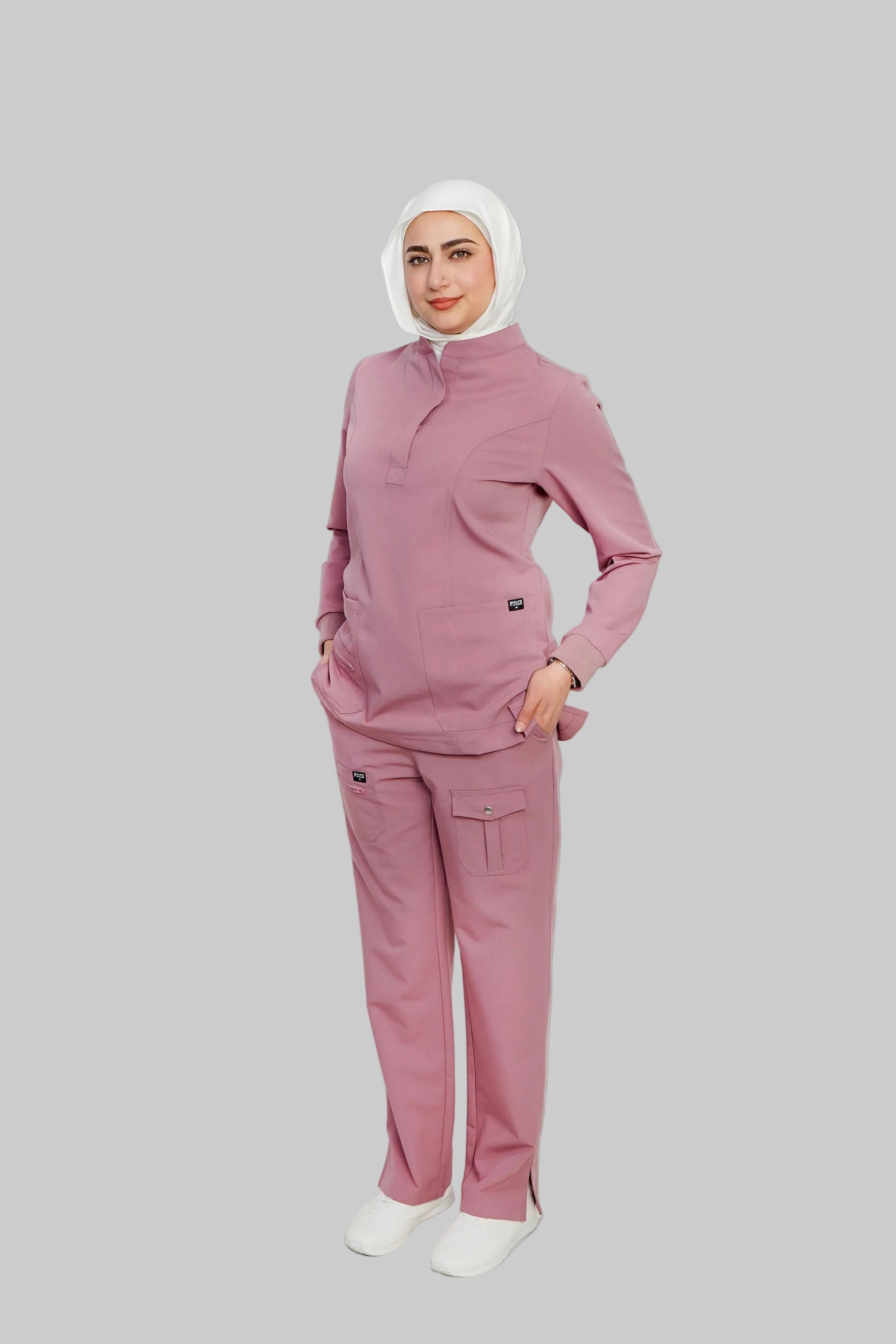 Person wearing a pink outfit with a white hijab on a light gray background