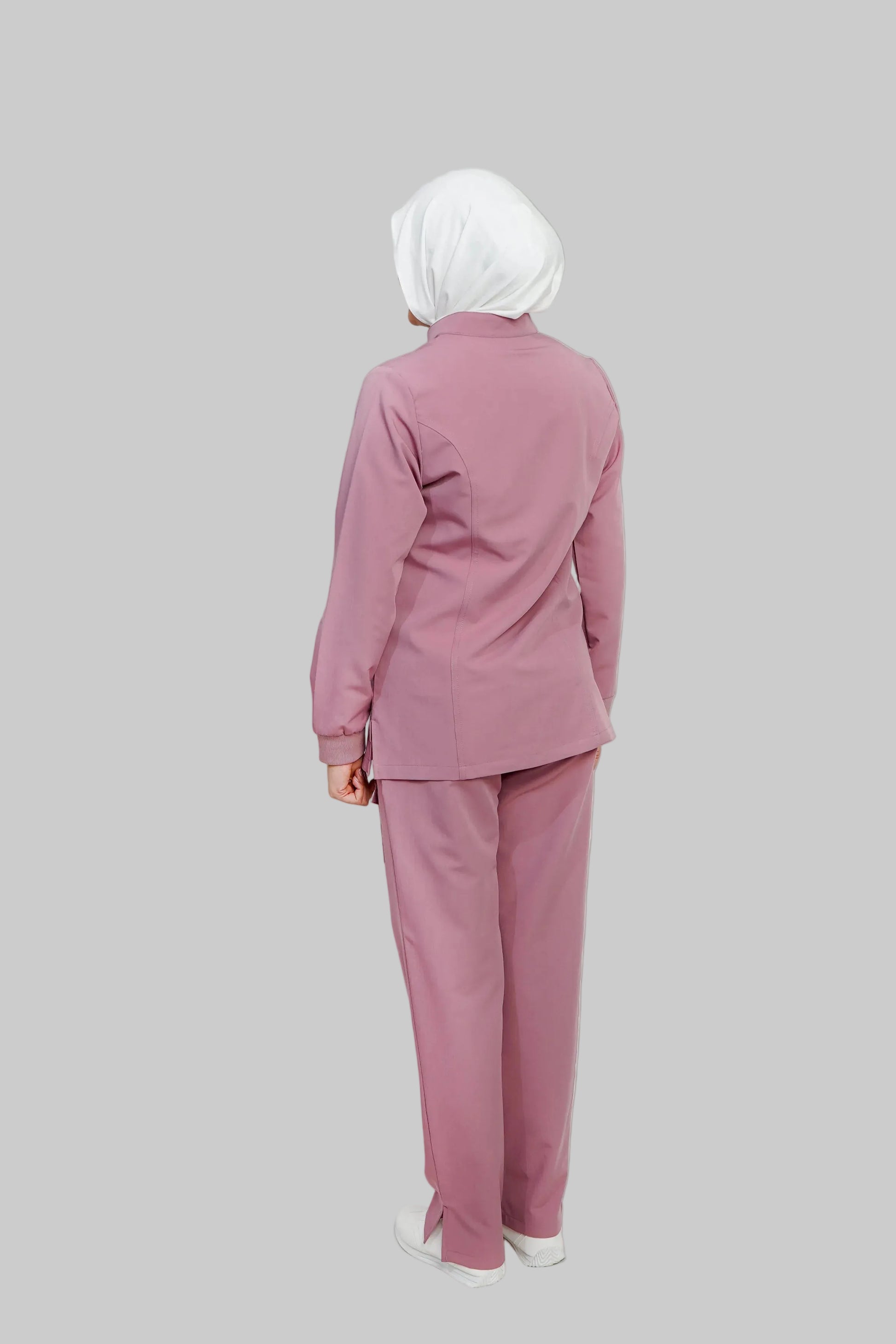Person wearing a pink outfit with a white hijab on a light gray background